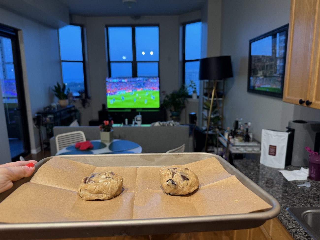 A tray of Everything dough held up, a football game on the television behind